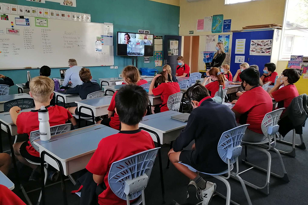 A classroom of students sitting at their desks looking at a screen 