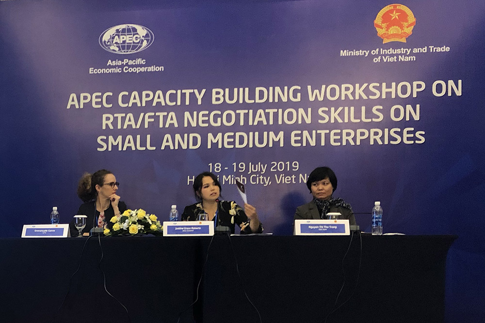 Justine speaking as part of a panel with two others with a sign behind them reading APEC Capability Workshop 