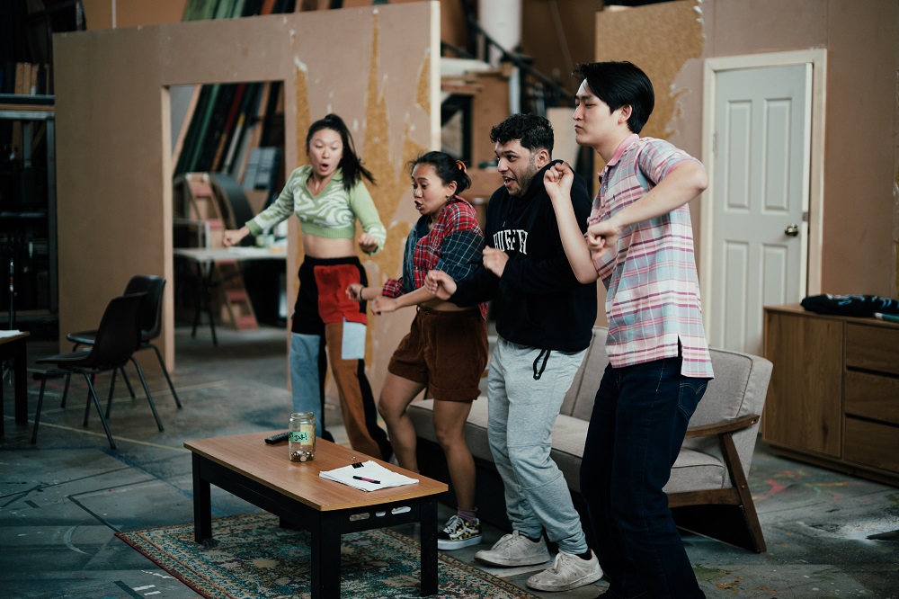 Four people dancing on a theatre set made up to look like a living room