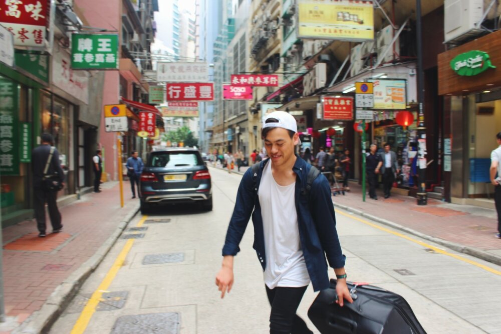 Sam Brosnahan pulling his luggage across a busy Hong Kong street