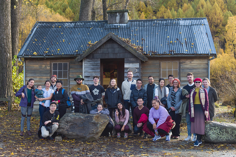 A group shot of Leadership network members in front of an old cottage in Otago, with autumn trees in the background