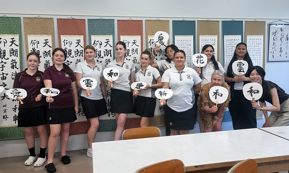 The Waihi group in a classroom holding paper fans with Japanese caligraphy on them