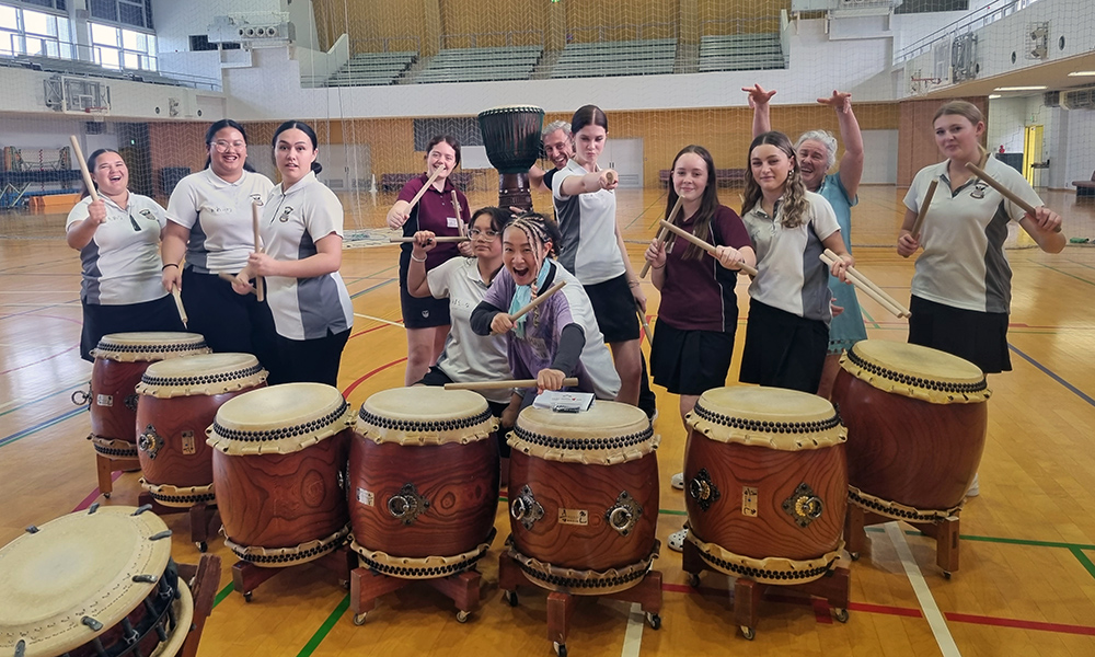 The Waihi College students in a gym holding drum sticks in front of taiko drums