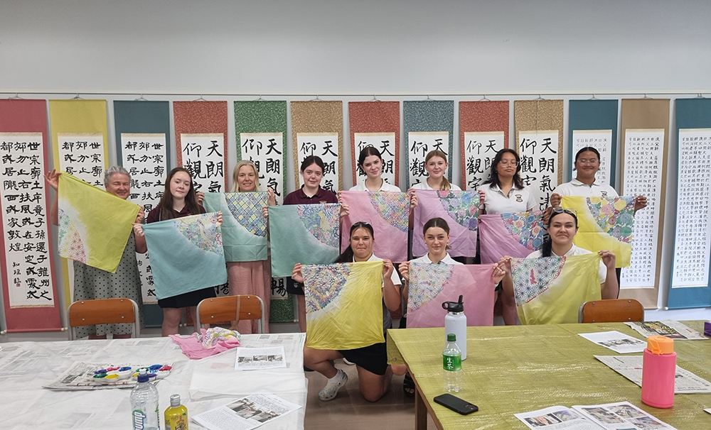 The Waihi College students holding up pieces of silk with patterns on it in a classroom