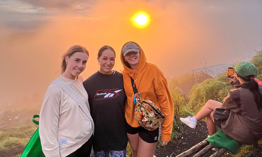 Cassidy posing for a photo with fellow intern Harriet Yeoman and a friend, with the sun set/rise behind them