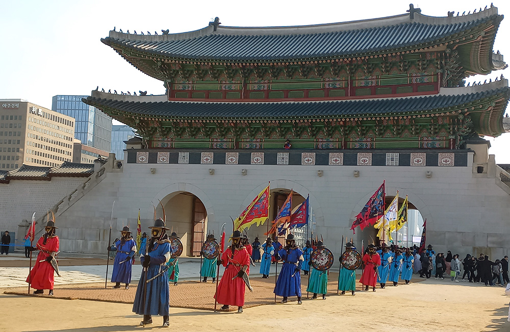 The changing of the guards ceremony with guards dressed in traditional Korean clothes marching with flags in front of a large traditional building