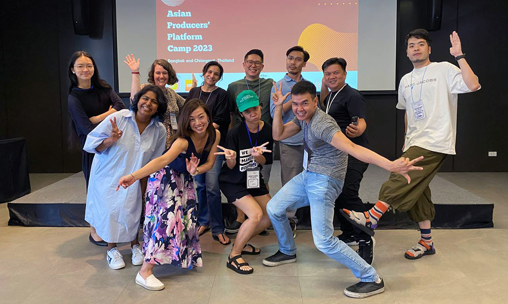 A grop of eleven people posing for a shot in front of a screen with the words Asian Producers Platform Camp 2023 projected on it