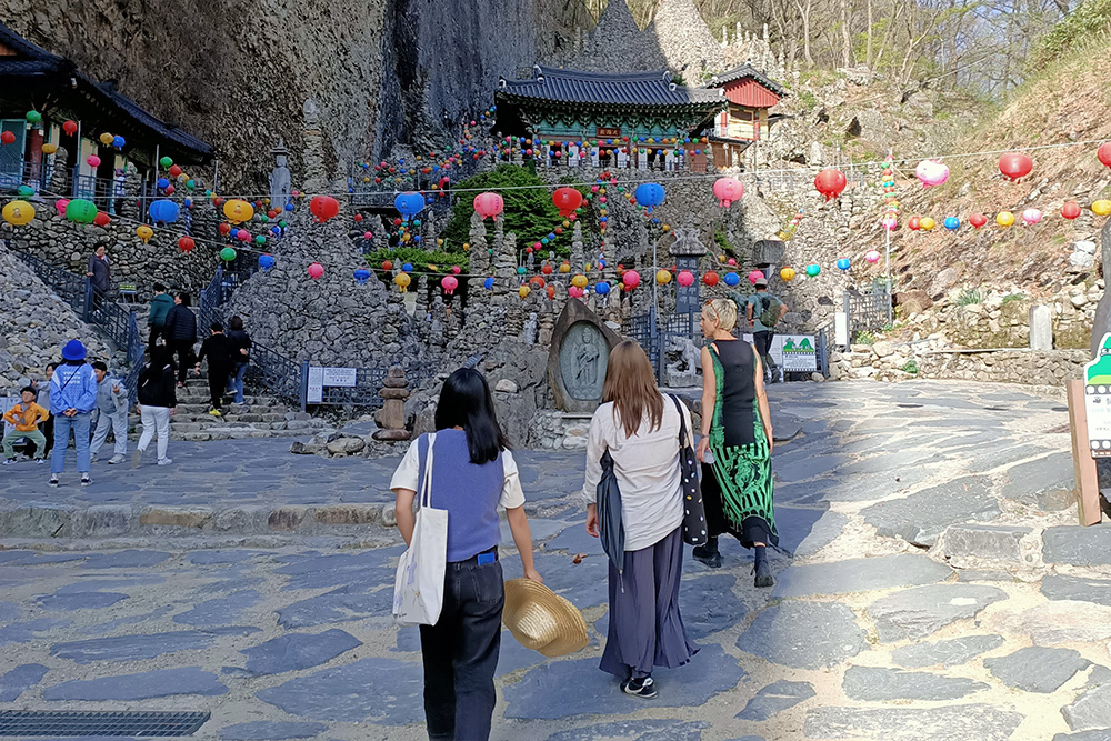 Three woman at an outside venue with stone buildings surrounded by cliffs and adorned with colourful paper lanterns