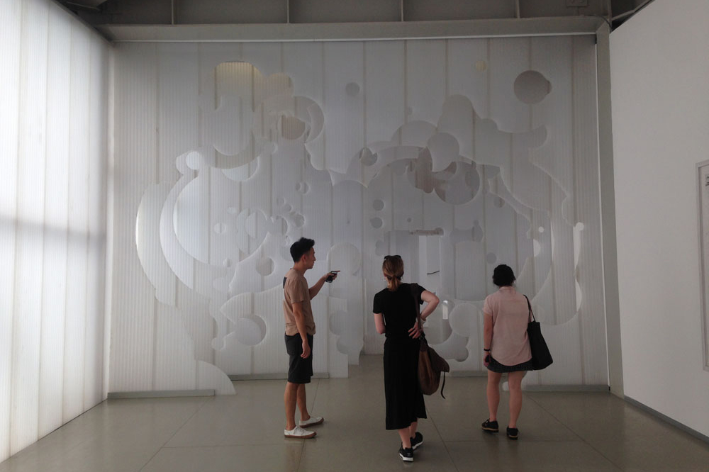 Three curators ooking at an abstract art work made of a translucent white material