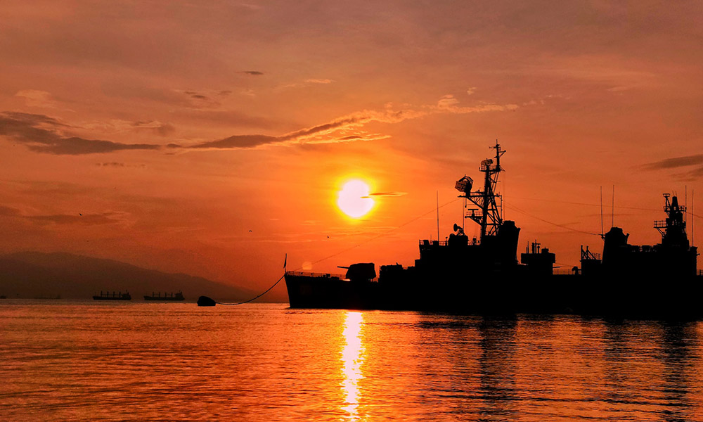 A destryoer at anchor with the sun rising in the background