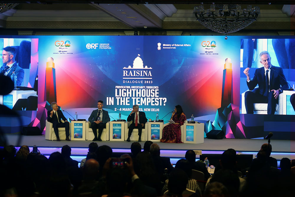 Four people sitting on chairs on stage at the Raisina Dialogue with an audience watching