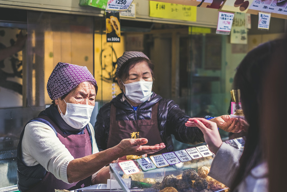 Two women wearing masks while serving customers from a street stall