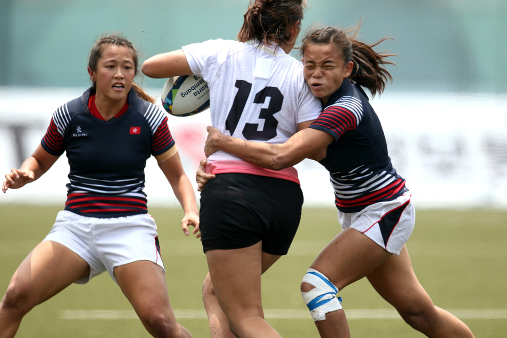 Three girls playing rugby, with on tackling another