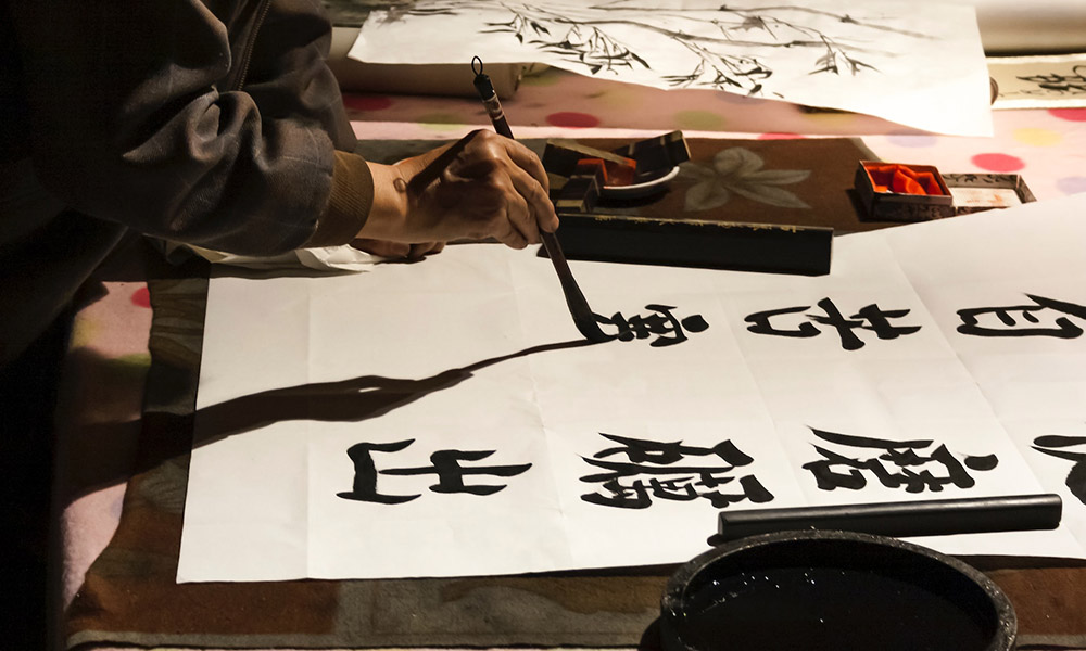 A person's hand using a calligraphy brush to write Chinese characters