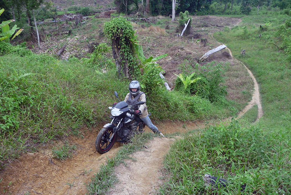 Nathan pushing a motorcycle up a dirt track in a rural area