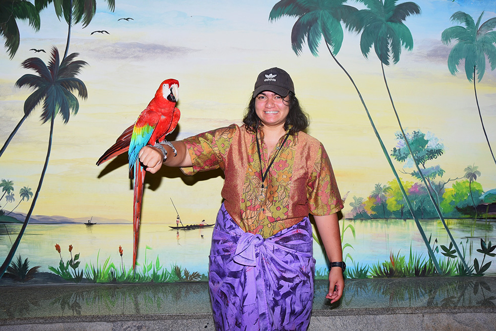 Pepe standing in front of a painted mural with a macaw parrot on her arm