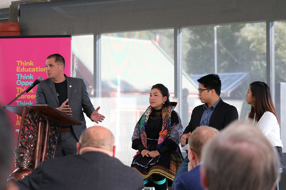 Luke Rikiti addressing an audience from a lectern with three of the Southeast Asian entrepreneurs beside him