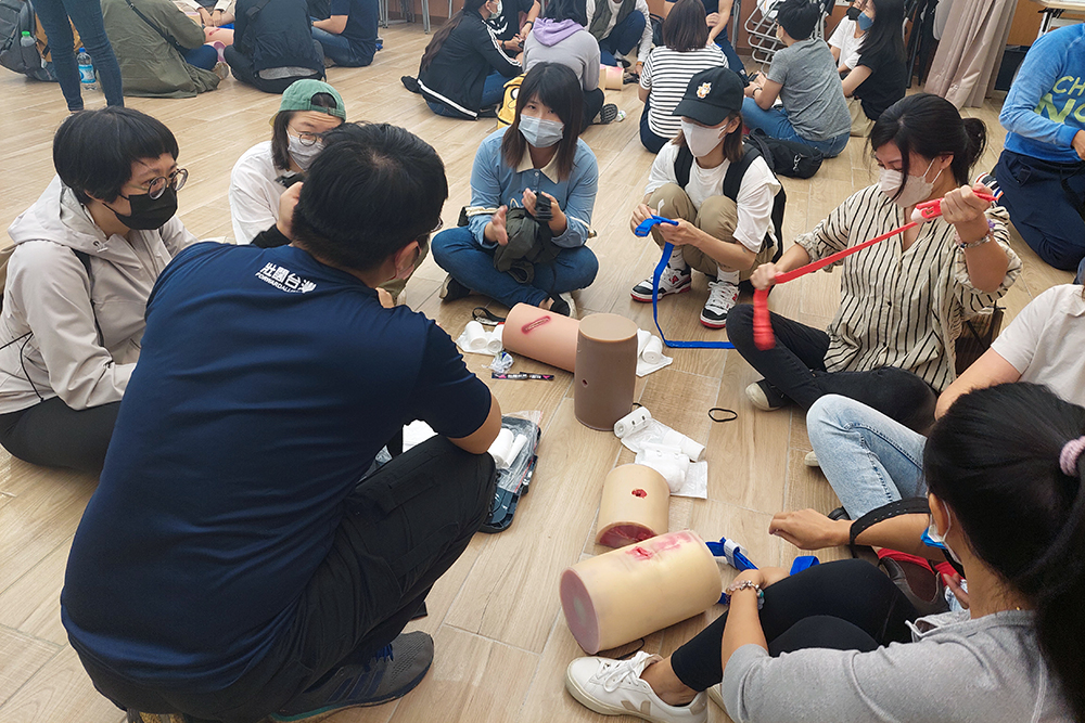 A group of Young people sitting on the ground how to pack trauma wounds on plastic dummies