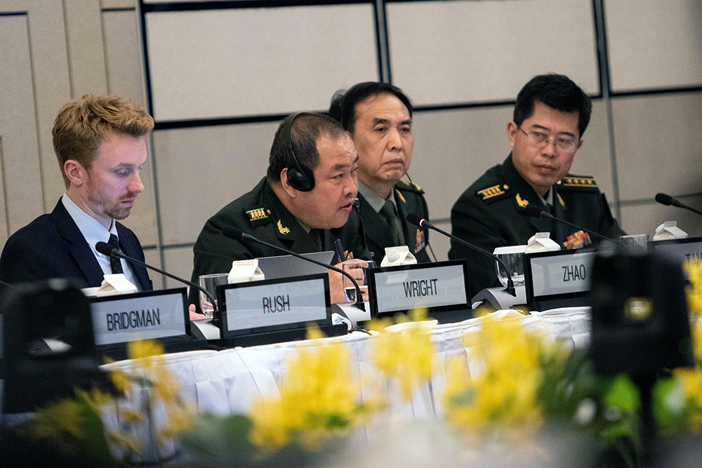A man in Chinese military uniform sitting at a table addressing a room