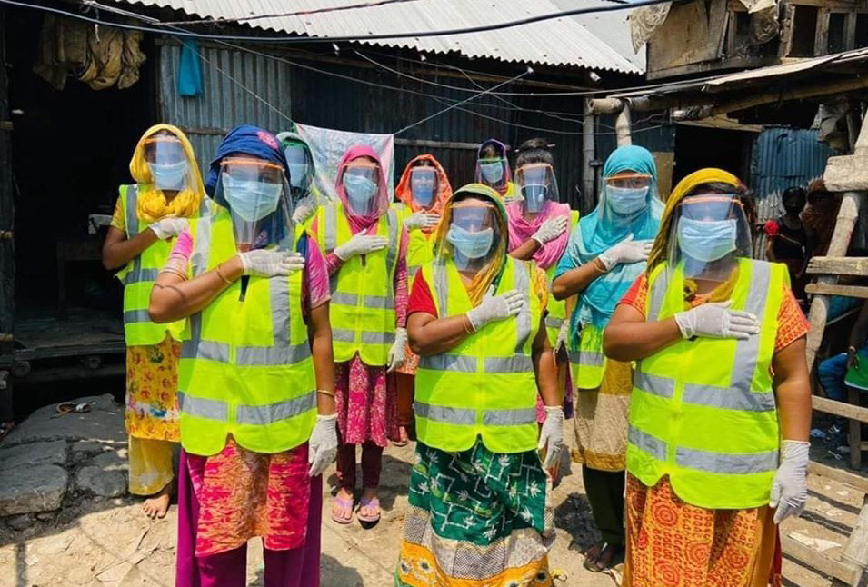Women in a refugee camp wearing protective garments including masks and high-vis vests