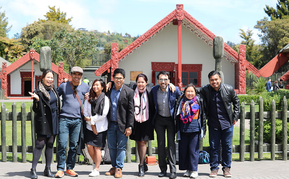 The eight entrepreneurs posing for a photo in front of the whare nui (meeting house) at Te Puia in Rotorua