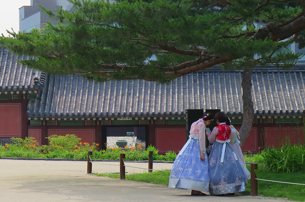 Three Korean women in traditional dress looking at a hand-held digital device